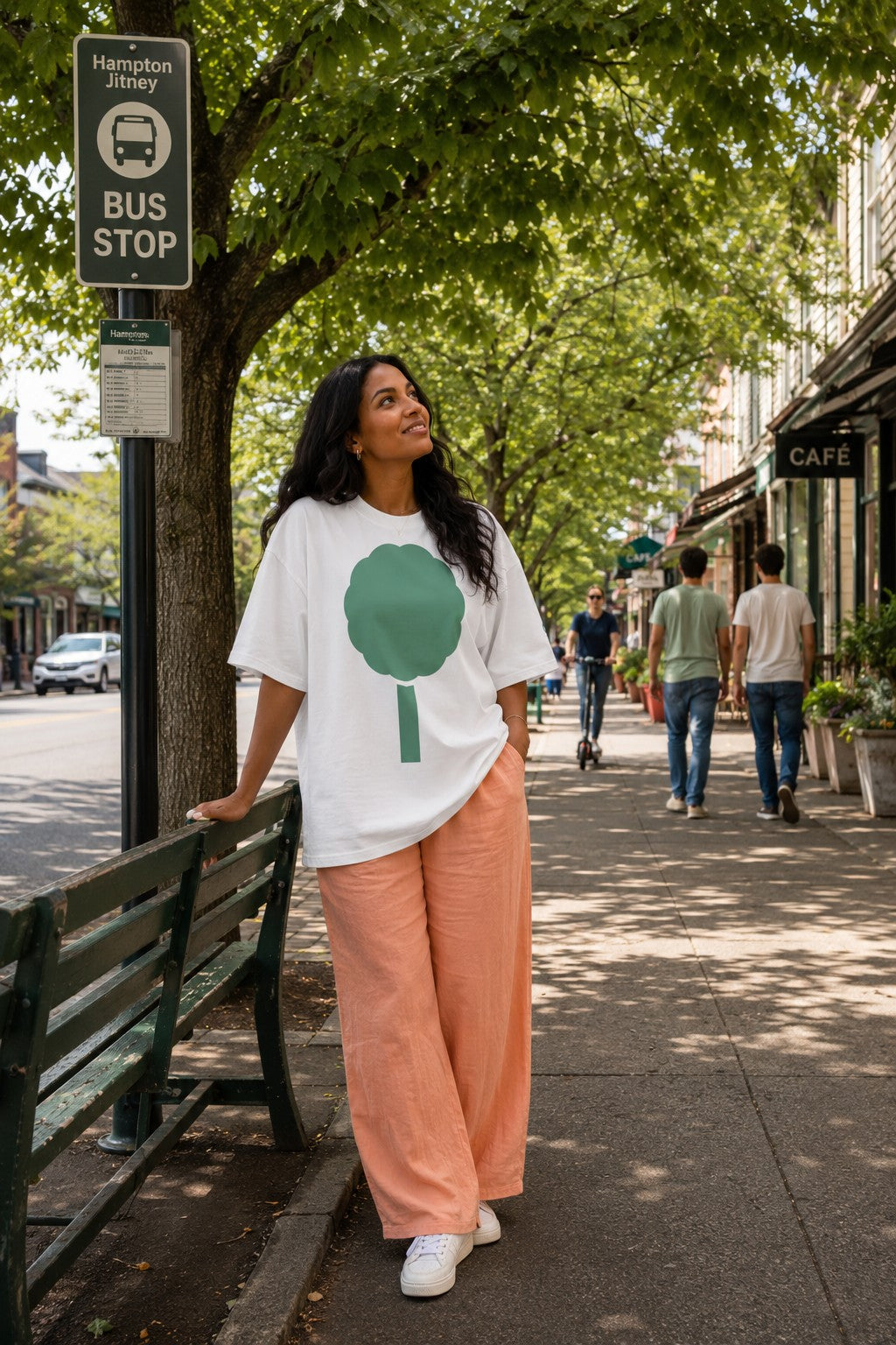 Darked hair woman. Sitting on wooden steps on a front porch in front of white wooden entry door. Dark green shutters. She is wearing a white t-shirt with a green leafy patter on the bottom of the shirt.