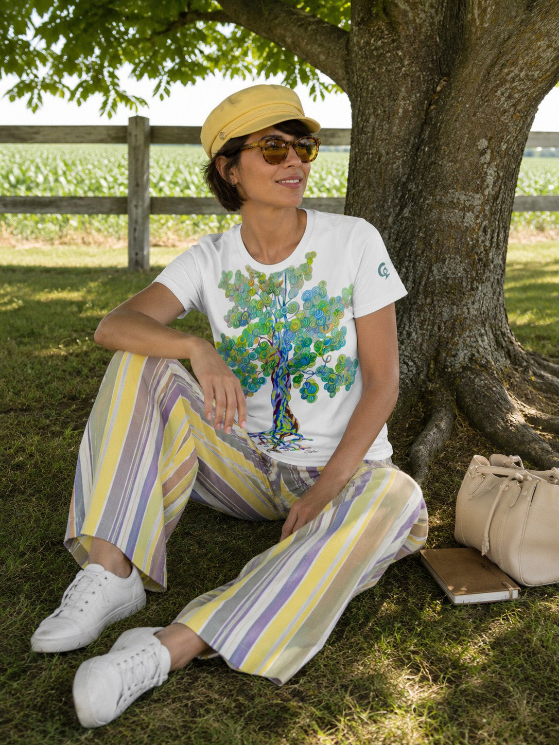 Darked hair woman. Sitting on wooden steps on a front porch in front of white wooden entry door. Dark green shutters. She is wearing a white t-shirt with a green leafy patter on the bottom of the shirt.