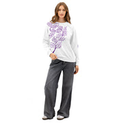 Woman wearing a white sweatshirt with a purple leaf design and gray pants on a white background