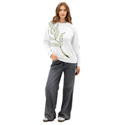 Woman wearing a white sweatshirt with a green leaf design and gray pants on a white background