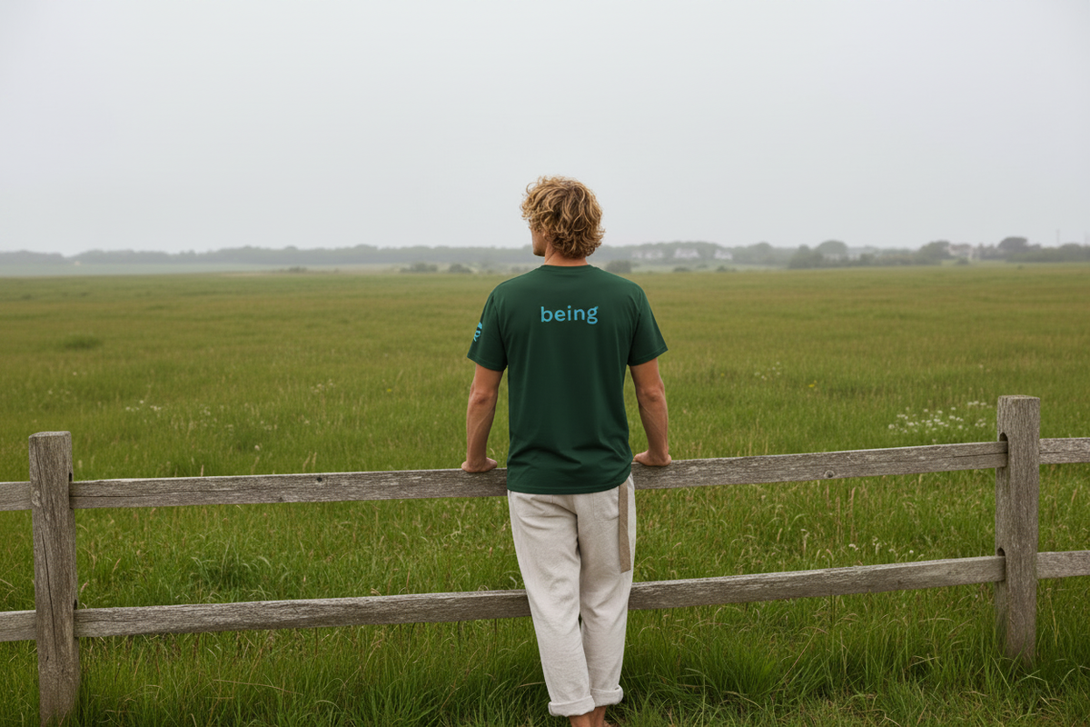 Man with dark green t-shirt standing at fence overlooking vast green field