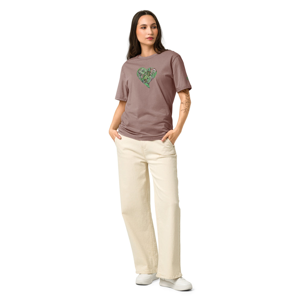 Woman wearing a blush colored t-shirt with a green graphic heart on a blush background